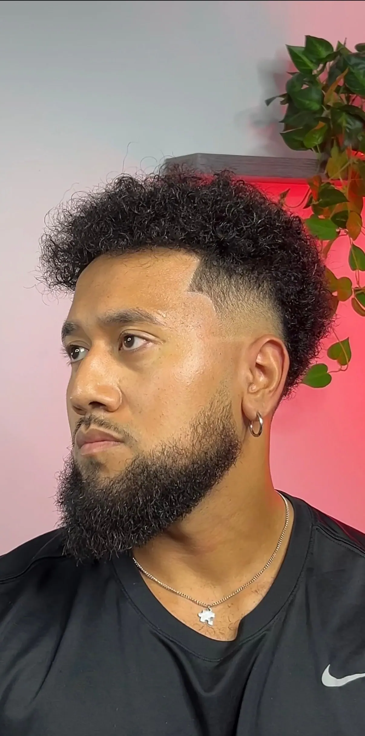 High curly top over a skin fade, cut through with a shaved part line and finished with a full beard.
