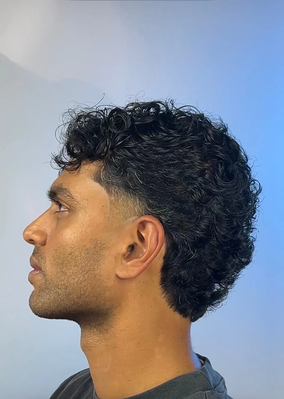 Loose curls left full from the crown through the back, cleaned up with a low taper at the ear.